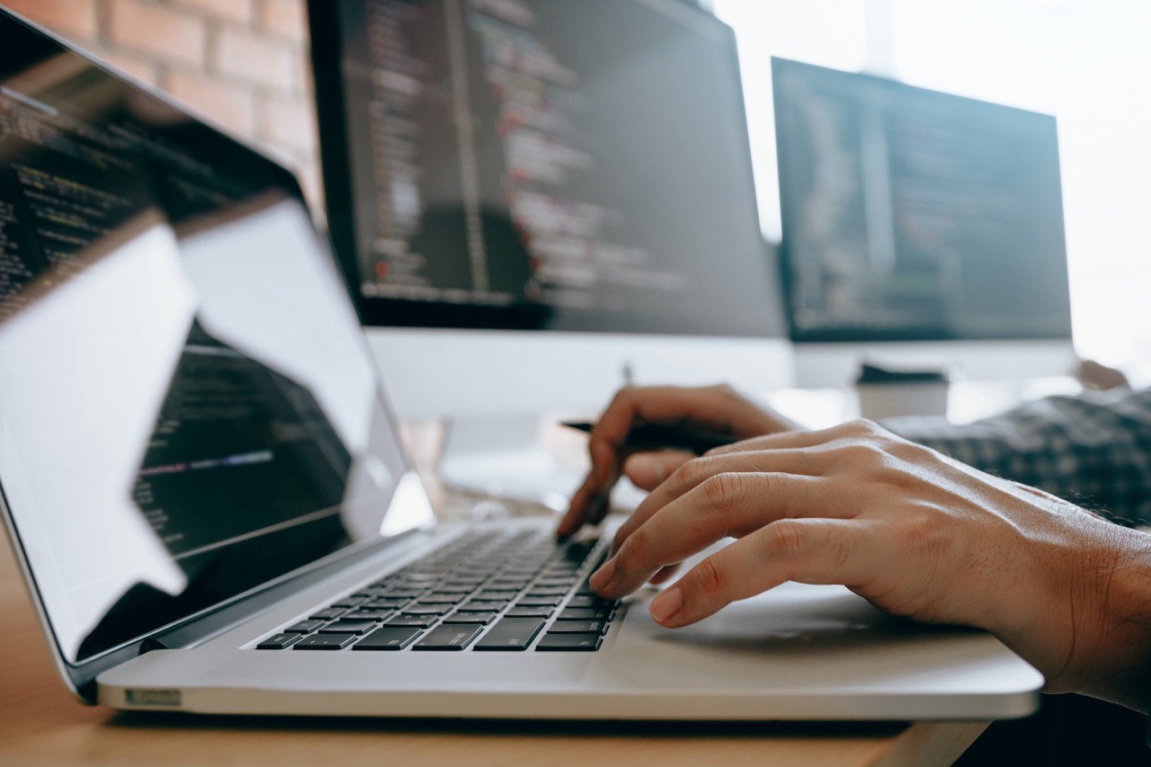 Entwicklungsarbeit am Laptop mit Code auf mehreren Bildschirmen