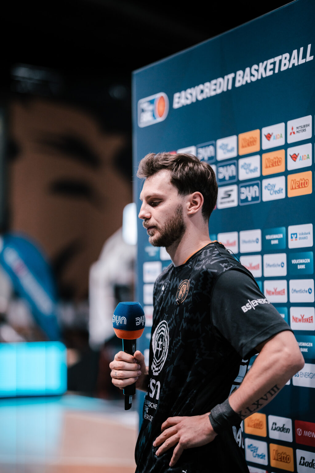 Reporter mit Mikrofon vor der Sponsorenwand bei den Basketball Löwen Braunschweig.