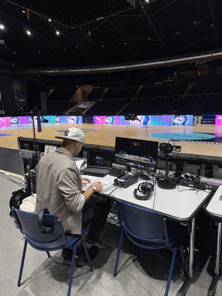 Produktionsarbeitsplatz mit Monitoren und einem Crewmitglied in der Basketballhalle.